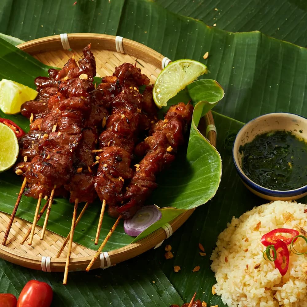 Grilled satay skewers glazed in sauce on a banana leaf with lime and chili, a Malaysian restaurant signature dish